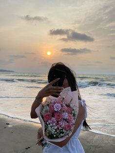 a woman taking a photo on the beach with her cell phone and flowers in front of her face