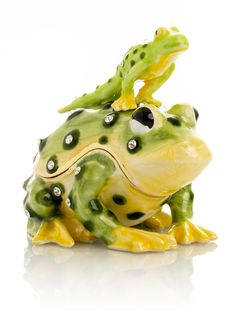 a ceramic frog figurine sitting on top of a white surface with green and yellow accents