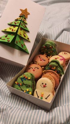 an open box filled with decorated cookies next to a christmas tree on a striped blanket