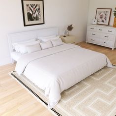 a white bed sitting on top of a wooden floor next to a dresser and mirror