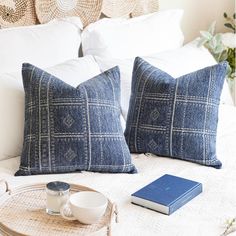 two blue pillows sitting on top of a bed next to a cup and saucer