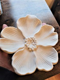 a person holding a white flower on top of a wooden table