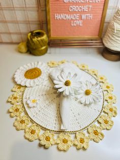 a crocheted doily with flowers on it and a sign in the background