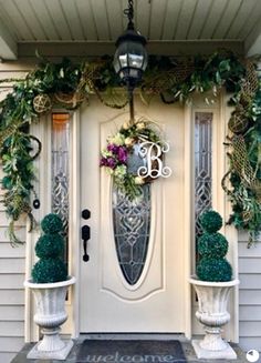 the front door is decorated with greenery and potted plants for an elegant look