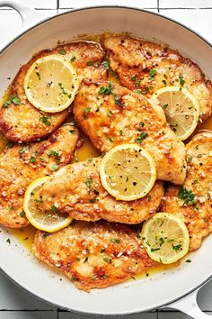 chicken with lemons and parsley in a skillet on a white counter top