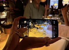 a person holding up a cell phone to take a photo of wine glasses on a table