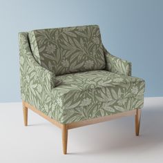 a green chair sitting on top of a white floor next to a blue wall and wooden legs