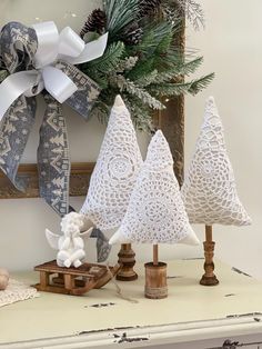 three white christmas trees are on a table with pine cones and ribbons in front of them