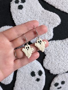 a hand holding two earrings with ghost faces on them