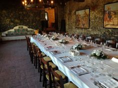 a long table set up with place settings and wine glasses on it in a stone walled dining room