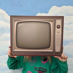 a woman holding up an old tv in front of her face with the sky painted on it