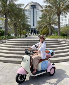 a man riding on the back of a pink and blue scooter next to palm trees