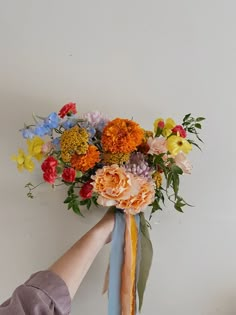 a person holding a bouquet of flowers on top of a white wall next to a blue ribbon