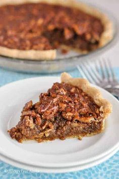 a slice of pecan pie on a white plate with a fork and blue table cloth