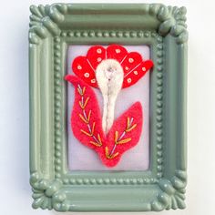 a red and white flower is in a green frame on the wall next to a gray framed object