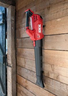 a red and black cordless drill is hanging on the side of a wooden wall