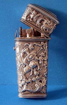 an ornately decorated metal container on a blue background, with the lid open to reveal its contents