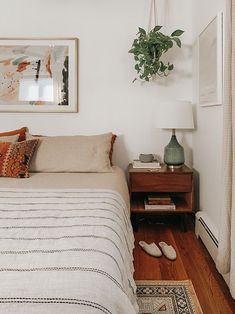 a bedroom with a bed, nightstand and plant on the wall above it in front of a window