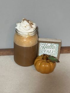 there is a small pumpkin next to a jar with whipped cream on it and a card