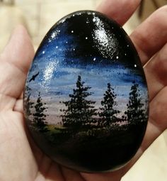 a hand holding a painted rock with trees and stars in the night sky on it