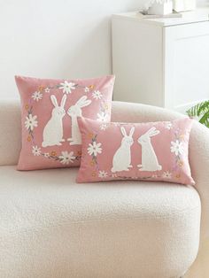 two pink pillows with white rabbits and daisies on them, sitting on a couch