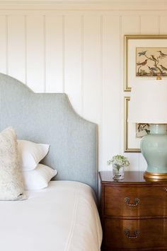 a blue vase sitting on top of a wooden dresser next to a white bedspread