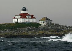 a lighthouse on top of a small island in the middle of the ocean with waves crashing around it