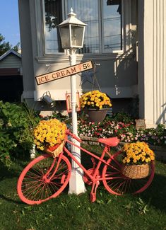 a red bicycle with baskets full of flowers sitting in front of a house