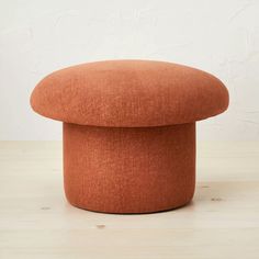 an orange round ottoman sitting on top of a wooden floor next to a white wall