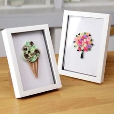 two framed pictures with flowers in them sitting on a wooden table next to each other