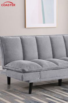 a gray couch sitting on top of a rug in front of a wall mounted painting