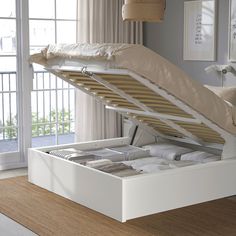 a white bed with an open drawer underneath it in a room next to a window