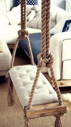 a chair that is hanging from a rope in the living room with pillows on it