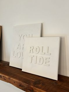 two white canvases with the words you are roll tide printed on them sitting on a wooden shelf