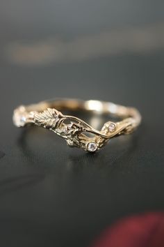 a gold wedding band with leaves and diamonds on the side, sitting on a black surface