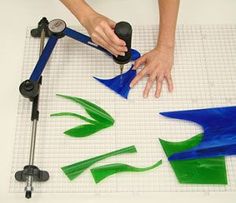 a person is making stained glass pieces on a white table with a blue and green design