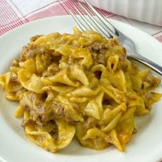 a white plate topped with pasta and meat covered in sauce next to a fork on a red and white checkered table cloth