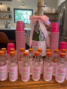 a table topped with lots of bottles of pink liquid next to stacks of paper cups