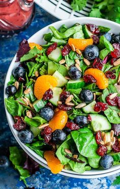 a salad with oranges, blueberries and spinach in a white bowl on a table