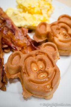 some waffles with faces on them are sitting on a plate next to eggs and bacon