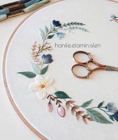 a pair of scissors sitting on top of a embroidery hoop with flowers and leaves around it