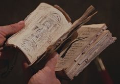 an old book being held by two hands with writing on the pages and in between