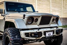 a white jeep parked in front of a building with its lights on and the hood off