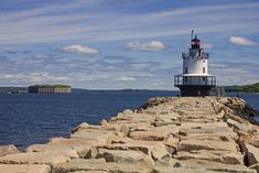 a light house sitting on top of a stone pier next to the ocean under a cloudy blue sky