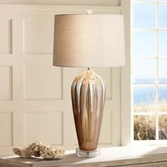 a table lamp sitting on top of a dresser next to a window with an ocean view