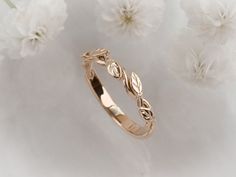 a gold wedding band with leaves on it and white flowers in the background, close up