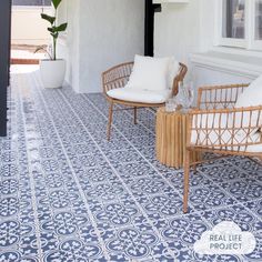 two wicker chairs sitting on top of a blue and white tile covered porch next to a potted plant