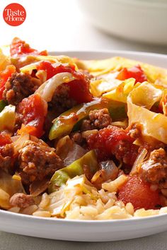 a white bowl filled with pasta and meat on top of a table next to a fork