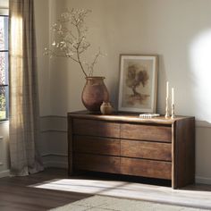 a wooden dresser sitting next to a window in a room with white walls and wood flooring