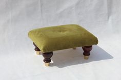 a small foot stool with wooden legs and a green cushion on the top, against a white background